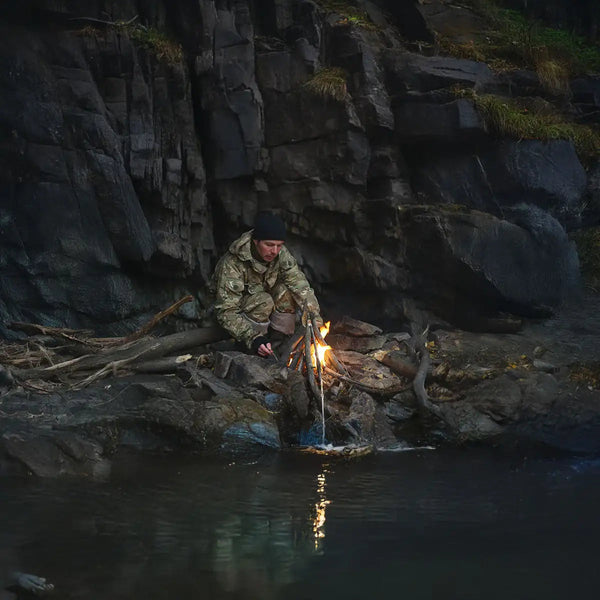 Mann sitzt am Ufer und macht Feuer.