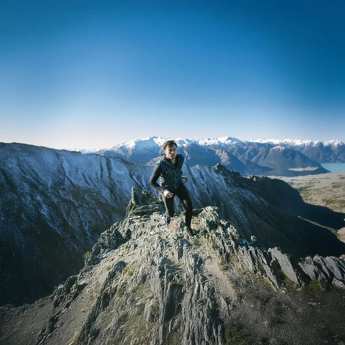 Eine Person auf einem Berggipfel und im Hintergrund verschneite Berge.
