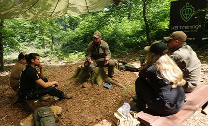 Vier Personen hören einem Survival-Trainer zu im waldigen Gebiet.