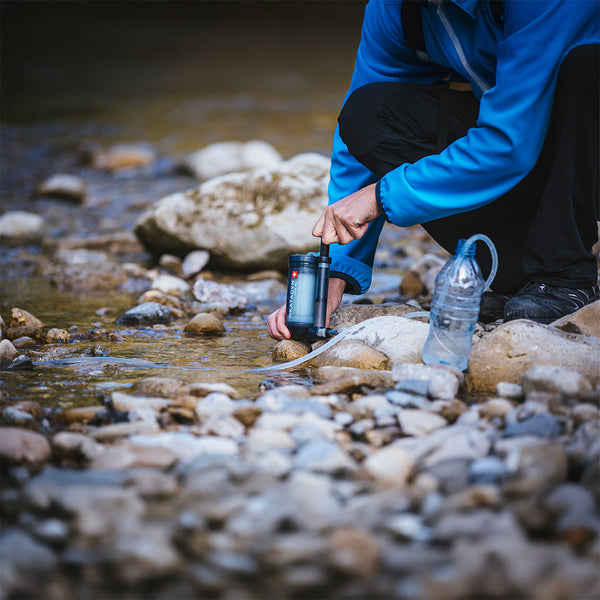 Ein Mensch benutzt ein Wasserfilter am Flussrand, während er an dem Wasser kniet.